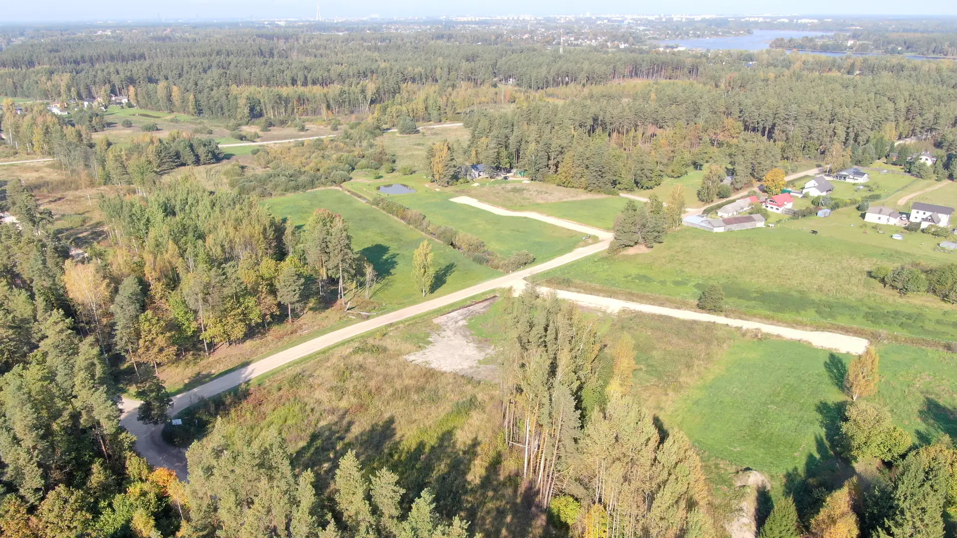 Krogsils no augšas rudenī: kvartāla grants ielas pie priežu meža, tālāk Rimdžūnu iela un kaimiņu mājas, pie horizonta Daugava un Rīga